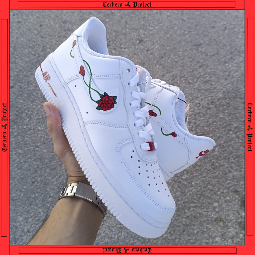 White Nike Air Force 1 with red rose and green vine details, held in hand