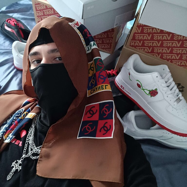 Artist in a hood and mask surrounded by custom rose-themed sneakers and Vans boxes