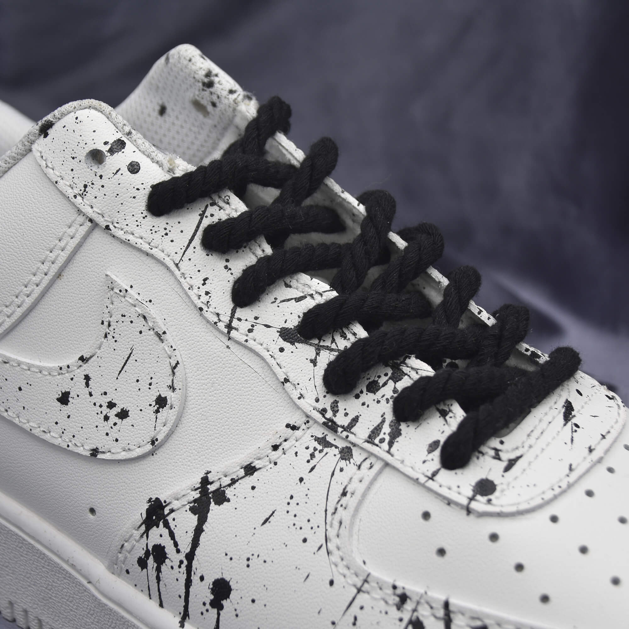 Black rope laces on white sneakers with black paint splatter