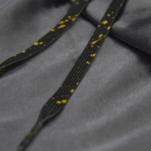 Black shoelaces with yellow paint splatter, placed on a gray satin background
