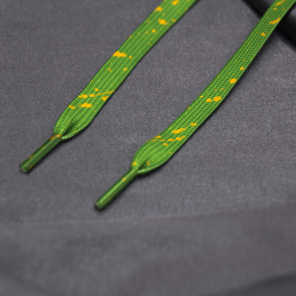 Green shoelaces with yellow paint splatter on gray fabric