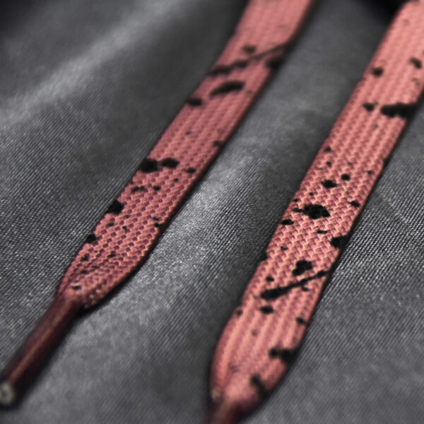 Pink shoelaces with a black paint splatter design on a satin background