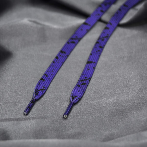 Deep purple shoelaces with a black splatter design on a gray fabric backdrop