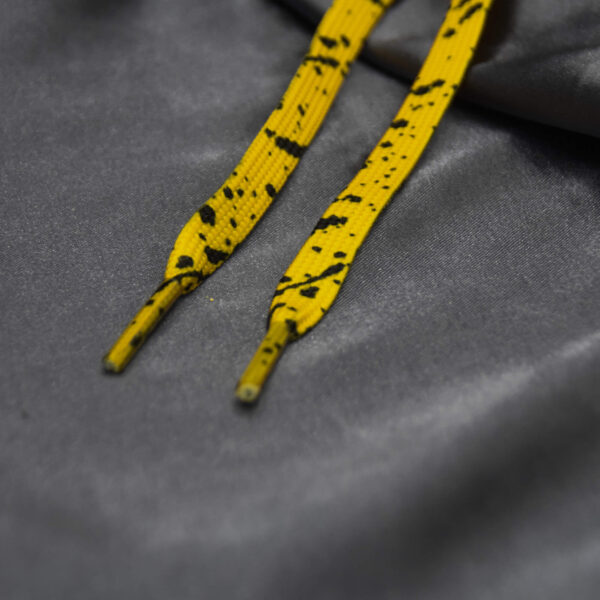 Yellow shoelaces with black paint splatter on a gray satin surface